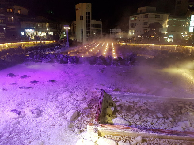 Blick auf Salzablagerungen der heißen Quellen; im Hintergrund die Stadt bei Nacht