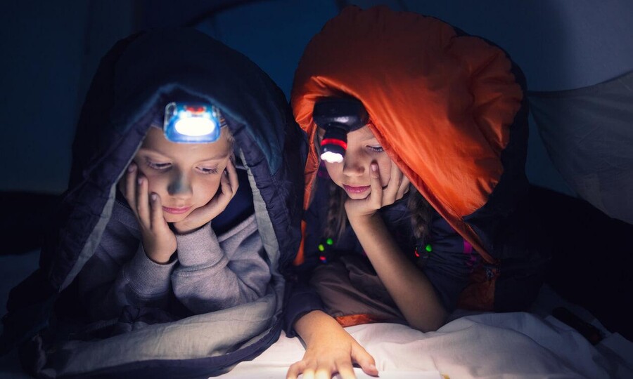 Zwei Kinder mit Stirnlampe lesen ein Buch