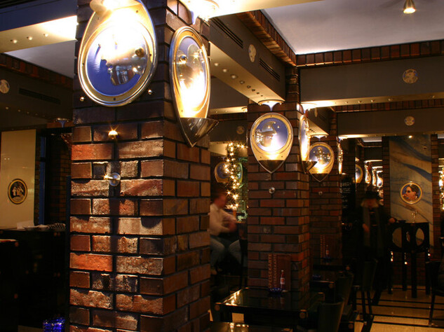 Innenraum mit Backsteinpfosten und runden beleuchteten Bilder auf denen Gesichter sind 