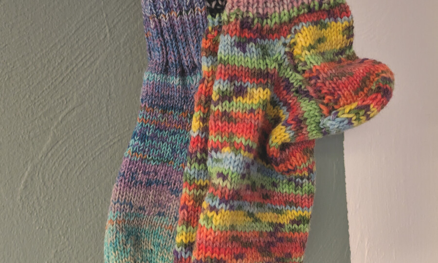 Bunte, selbstgestrickte Socken, die vor einer Wand hängen