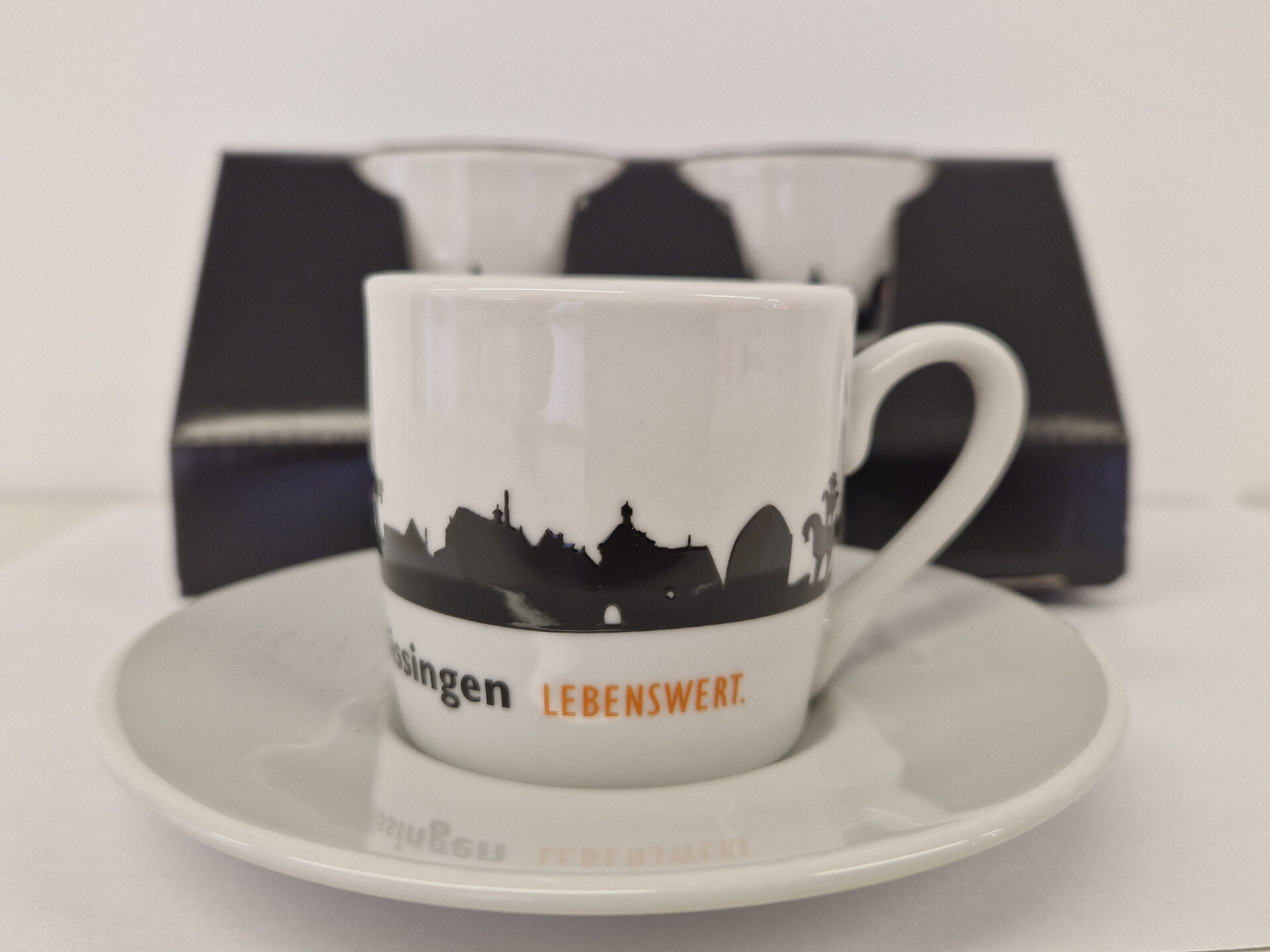Espressotasse Bi-Bi 2er Set (25,00 €) Eine weiße Espressotasse steht auf dem Unterteller. Auf der Tasse ist eine schwarze Stadtsilhouette zu sehen.