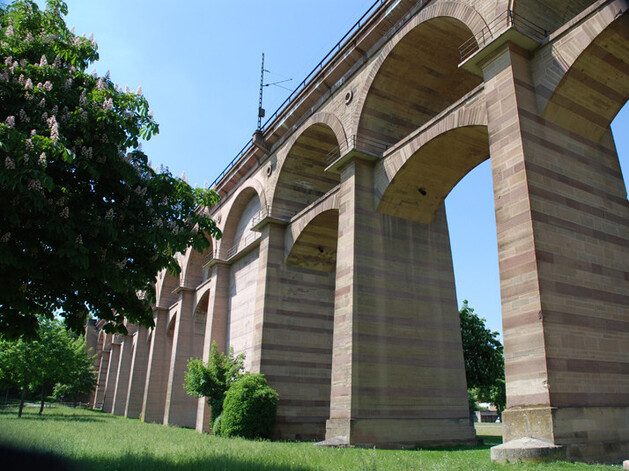 Brücke mit vielen Bögen darunter ein Wiese mit Bäumen