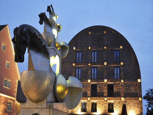 Perdeskulpturen vor beleuchtetem Backsteinhaus