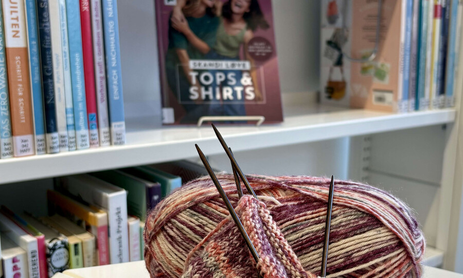 Strickprojekt mit Wollknäul vor Büchereiregal