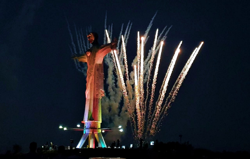 Bunt beleuchtete Statue "Christo Rey del Valle" bei Nacht mit Feuerwerk